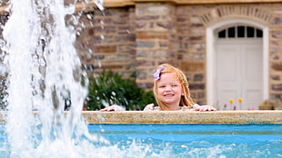 girl with brown hair smiling next to a outdoor fountain